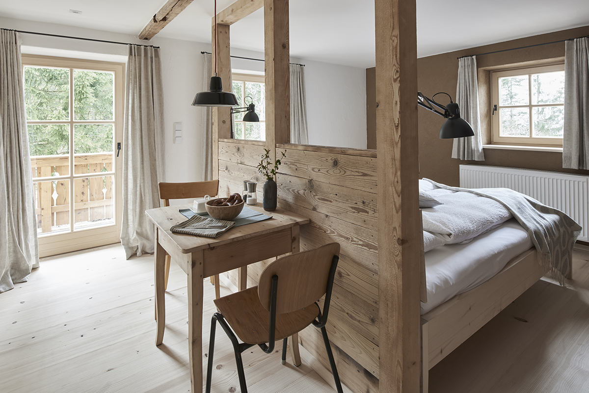 Essplatz mit Emaille-Lampe und Raumtrenner Ein kleiner Essplatz mit Holztisch und zwei Stühlen. Darüber hängt eine Emaille-Lampe. Eine halb-offene Trennwand aus Holz trennt den Essbereich vom Schlafzimmer