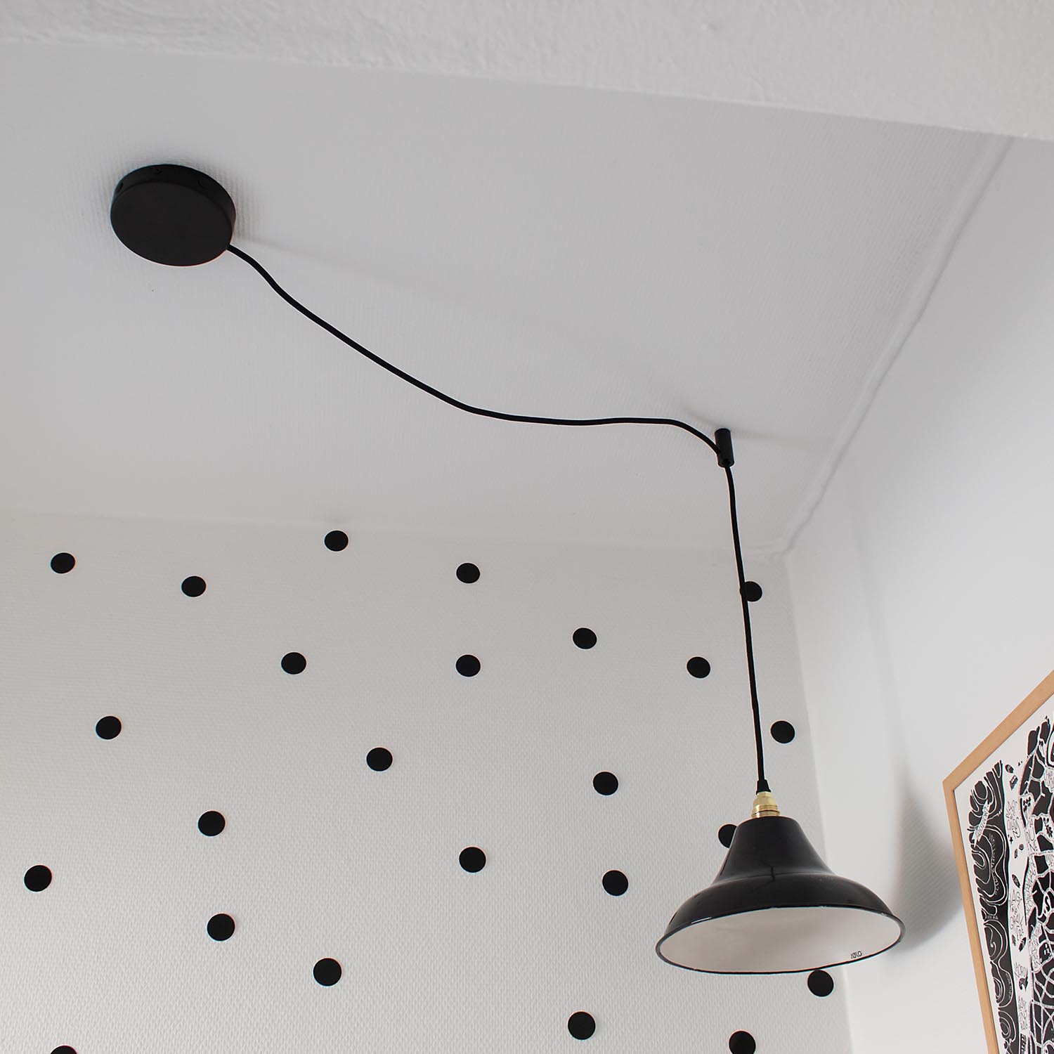 Lampe mit Affenschaukel eine schwarze Lampe, die von der Decke hängt vor einer Wand mit Punktemuster