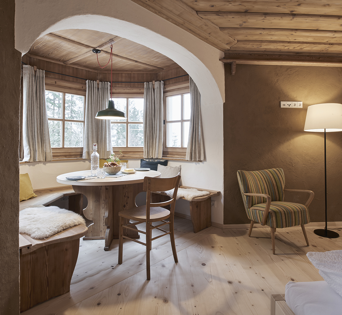 Essplatz mit Emaillelampe Ein Erker in einem alten Bauernhaus. Im Erker befindet sich ein runder Holztisch mit einer Eckbank und einem Holzstuhl. Über dem Tisch hängt eine alte Fabriklampe