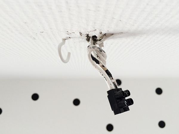 Stromanschluss an der Decke Zimmerdecke mit Stromkabeln, die aus der Decke kommen sowie einem Haken, der in die Decke geschraubt ist, um eine Lampe daran aufzuhängen